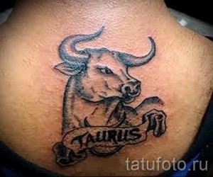 Фото тату: черно-серая татуировка головы быка с надписью "TAURUS" на свитке, расположенная на шее, классический стиль.