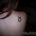 Фото готовой тату знак зодиака телец - черный символ на правой лопатке у молодой девушки