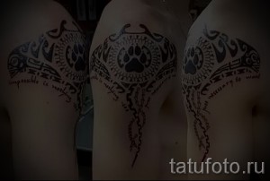 Фото тату манта-рей на плече с добавлением отпечатка лапы волка и мотивирующей надписи. Черно-белый рисунок татуировки в полинезийском стиле.