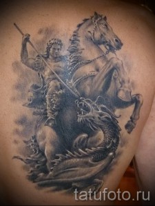 Фото тату Георгия Победоносца на лопатке, выполненное в реалистичном стиле с использованием черно-серых оттенков. Детализированный рисунок татуировки.