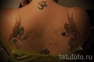 Фото татуировки с изображением двух ярких фей на спине девушки. Феи с разноцветными крыльями и детальной прорисовкой.