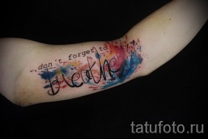 Фото тату: красивая акварельная татуировка с надписью "Don't forget to breathe" и красочными брызгами, расположенная на предплечье.