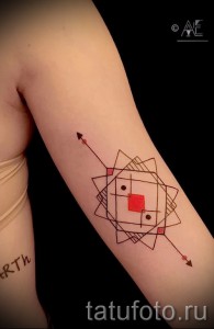 Фото тату: абстрактный геометрический рисунок на руке, состоящий из красных и коричневых линий, образующих ромбовидную структуру с красным квадратом в центре.