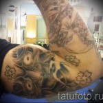 Фото тату на плече: череп, украшенный ветками цветущей сакуры в японском стиле. Использованы оттенки серого, черного и розового.
