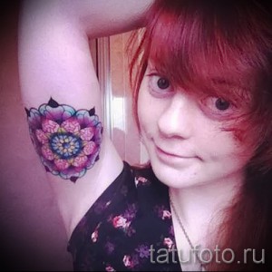 Фото тату: яркая и детализированная татуировка в виде мандалы на плече девушки. Пастельные тона, геометрический узор.