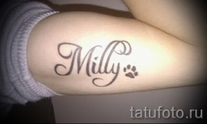 Фото тату: надпись "Milly" и отпечаток лапки, выполненные на руке девушки. Нежный и минималистичный дизайн.