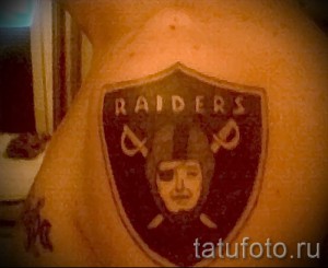 Фото тату на руке с изображением щита с логотипом команды Las Vegas Raiders, выполненного в черно-белых тонах.