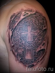 Фото тату на плече: щит с кельтским крестом, выполненный в технике blackwork. Рисунок детализированный, с использованием сложных кельтских узоров.