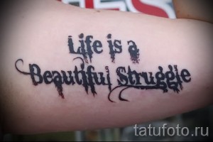 Фото тату: надпись 'Life is a Beautiful Struggle' на предплечье мужчины. Шрифт выполнен в грубом, небрежном стиле.