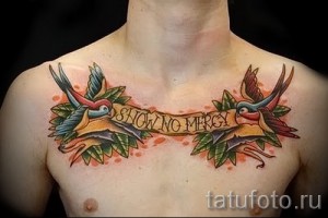 Фотография татуировки двух ласточек, держащих ленту с надписью 'SHOW NO MERCY', выполненной на груди. Яркий и красочный рисунок в стиле олд скул.