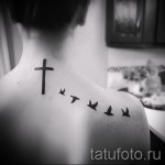 Фото тату нескольких ласточек, летящих к кресту на спине. Черно-белый рисунок татуировки в графическом стиле.