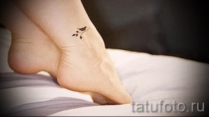 Фото тату: маленькая татуировка птички с веточкой на лодыжке. Нежный и минималистичный рисунок татуировки.
