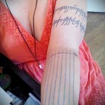 Фото тату: Длинная надпись, выполненная в стиле эльфийской вязи, опоясывает предплечье. Татуировка выполнена в черном цвете с тонкими линиями.