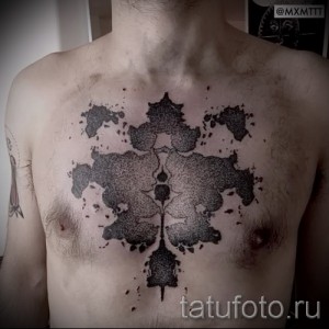 Фото тату на груди мужчины с абстрактным рисунком из черных пятен и текстур, выполненным в технике дотворк.