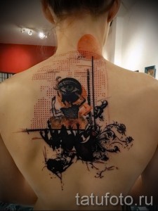 Фото татуировки на спине с изображением девушки с закрытыми глазами и третьим глазом на лбу, окруженной абстрактными элементами и брызгами краски.