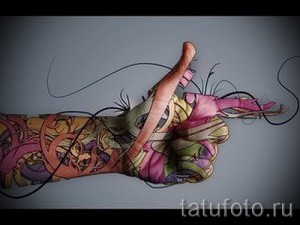 Фото яркой татуировки на руке, изображающей цветочный орнамент. Рисунок выполнен в розовых, зеленых и желтых тонах.