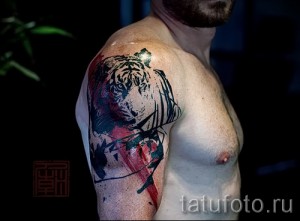 Фото тату акварельного тигра на плече. Черные линии, брызги краски, реалистичный взгляд. Идеально для тех, кто ценит художественный стиль и дикую природу.