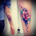 Фото тату: акварельный рисунок цветка на руке. Яркие розовые, голубые и фиолетовые оттенки, размытые контуры, создающие эффект акварели.