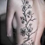 Фото татуировки с изображением ветви сакуры на боку. Выполнена в черно-белой гамме, с акцентом на детализацию и плавные линии.