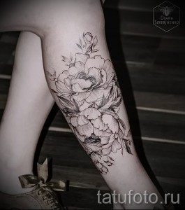Фото татуировки с изображением пышных пионов на икре. Выполнена в технике blackwork, с акцентом на детализацию и тени.