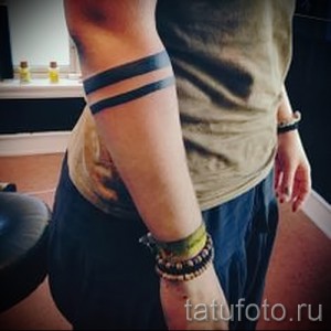 Фото тату: Две параллельные черные полосы, обернутые вокруг предплечья, создают минималистичный и стильный браслет. Татуировка выполнена в графическом стиле.