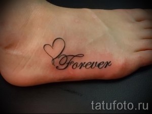 Фото милой татуировки с надписью 'Forever' и маленьким сердцем на стопе, выполненной в черном цвете.