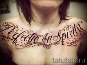 Фото тату надписи 'Perfectio In Spiritu' на груди, выполненной в классическом стиле с декоративными узорами.