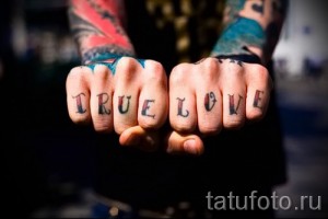Фото татуировки с надписью 'True Love' на костяшках пальцев, выполненной в классическом стиле с использованием красных и черных чернил. Подходит для романтиков.