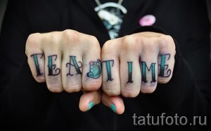 Фото яркой татуировки с надписью 'Tea Time' на костяшках пальцев, дополненной изображением милой мультяшной мышки. Подходит для любителей чая и оригинальных рисунков.