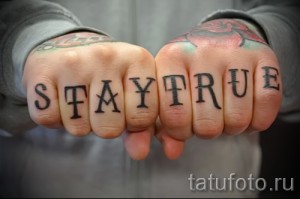 Фото тату с надписью 'STAY TRUE' на костяшках пальцев. Черные буквы, минималистичный дизайн, татуировка на руке, мотивационная надпись.