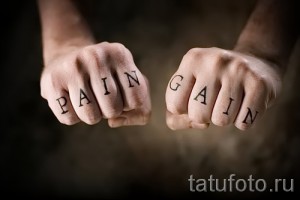 Фото тату с надписью 'PAIN GAIN' на костяшках пальцев. Черные буквы, минималистичный дизайн, татуировка на руке, мотивационная надпись.