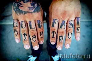 Фото тату с надписями 'HOLD FAST' и 'TRUE' на костяшках пальцев. Черные буквы с фиолетовым оттенком, татуировка на руке, морская тематика.