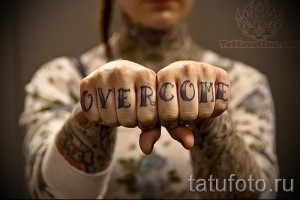 Фото тату с надписью 'OVERCOME' на костяшках пальцев. Черные буквы с легким оттенком, татуировка на руке, мотивационная надпись.