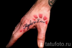 Фото татуировки с надписью "Fight to Live" на руке, выполненной каллиграфическим шрифтом с добавлением красных сердец.
