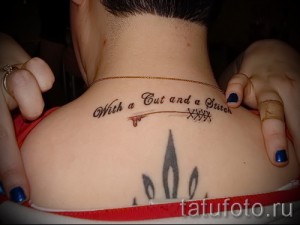 Фото тату на спине: надпись 'With a Cut and a Stitch' и стрела, пронзающая сердце. Оригинальный и символичный рисунок татуировки.