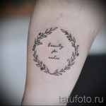 Фото тату: надпись "beauty for ashes" в круге из тонких веточек и цветов на женской руке. Нежный и символичный эскиз тату.
