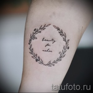 Фото тату: надпись "beauty for ashes" в круге из тонких веточек и цветов на женской руке. Нежный и символичный эскиз тату.