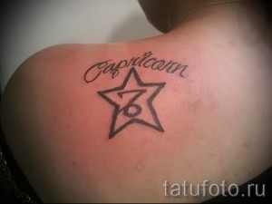Фото тату с изображением символа Козерога и звезды на плече женщины. Рисунок татуировки выполнен в черном цвете с элементами каллиграфии.