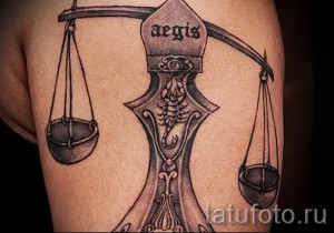Фото тату: сложная татуировка Весы со скорпионом на плече, выполненная в технике черно-белой татуировки с высокой детализацией и тенями.