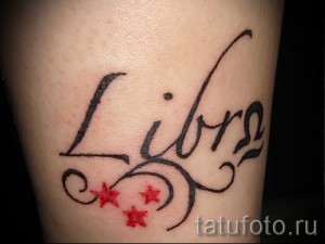 Фото тату Весы на лодыжке: надпись 'Libra' с символом знака зодиака и красными звездами.
