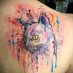 Фото тату: акварельный рисунок кошки с фиолетовыми оттенками на женской лопатке. Мягкие переходы цветов и нежные линии.