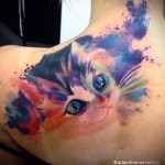 Фото тату: акварельный рисунок котенка с голубыми глазами на женской лопатке. Нежные переходы цветов и реалистичное изображение.