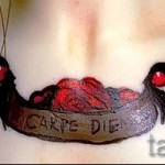 Фото тату лодки, полной черепов, с надписью 'Carpe Diem'. Рисунок выполнен в темных тонах с использованием красных акцентов.