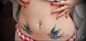 Фото тату двух ласточек на животе девушки. Небольшие, цветные татуировки в стиле олдскул с голубыми и черными оттенками. Идеи для тату.