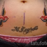 Фото тату двух ласточек в стиле олд скул на животе женщины с надписью 'No Regrets'. Яркий рисунок татуировки для вдохновения.