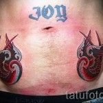 Фото тату: Две красные татуировки ласточек и надпись "JOY" на женском животе. Красочный и позитивный рисунок.