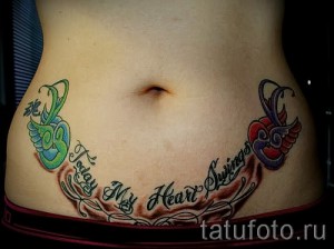 Фото тату: Цветная татуировка с двумя птицами, надписью "Today My Heart Sings" и декоративными элементами на женском животе.