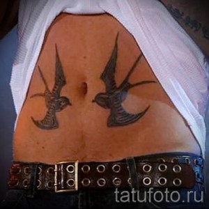 Фото тату двух ласточек в стиле графика на женском боку, выполненное в черном цвете с использованием тонких линий.