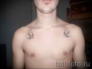 Фото двух татуировок ласточек, расположенных симметрично на груди мужчины. Черно-серый рисунок, выполненный в традиционном стиле.