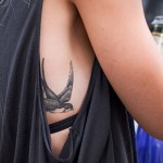Фотография минималистичной татуировки ласточки, выполненной в технике blackwork, на женском боку.